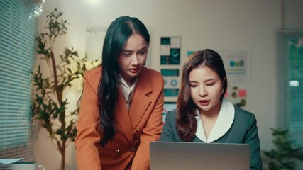 Poster - Two asian businesswomen are collaborating late at night in the office, discussing details on a laptop while analyzing strategies and planning their next steps in a professional environment