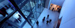 © David Giraud - Vue plongeante de l'entrée d'un immeuble des bureaux d'une entreprise, avec des gens franchissant les portes vitrées dans un flou de mouvement.