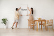 © Pixel-Shot - Young couple hanging poster on white brick wall in dining room, back view