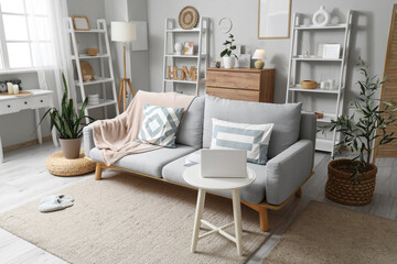 Interior of living room with stylish sofa, shelving units and laptop on coffee table