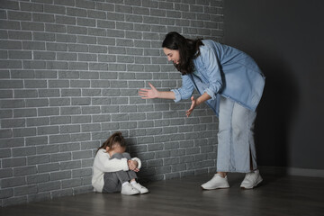 Wall Mural - Scared little girl with her angry mother sitting near grey brick wall. Domestic violence concept