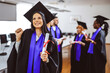 © Mediteraneo - Portrait of graduate student in toga holding her diploma in front of her friends.