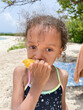 © Anya Brewley Schultheiss/Stocksy - Child with cute curly hair eating a mango while on a beach.