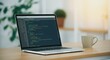 © Artiscia - Laptop displaying coding screen on wooden desk with mug