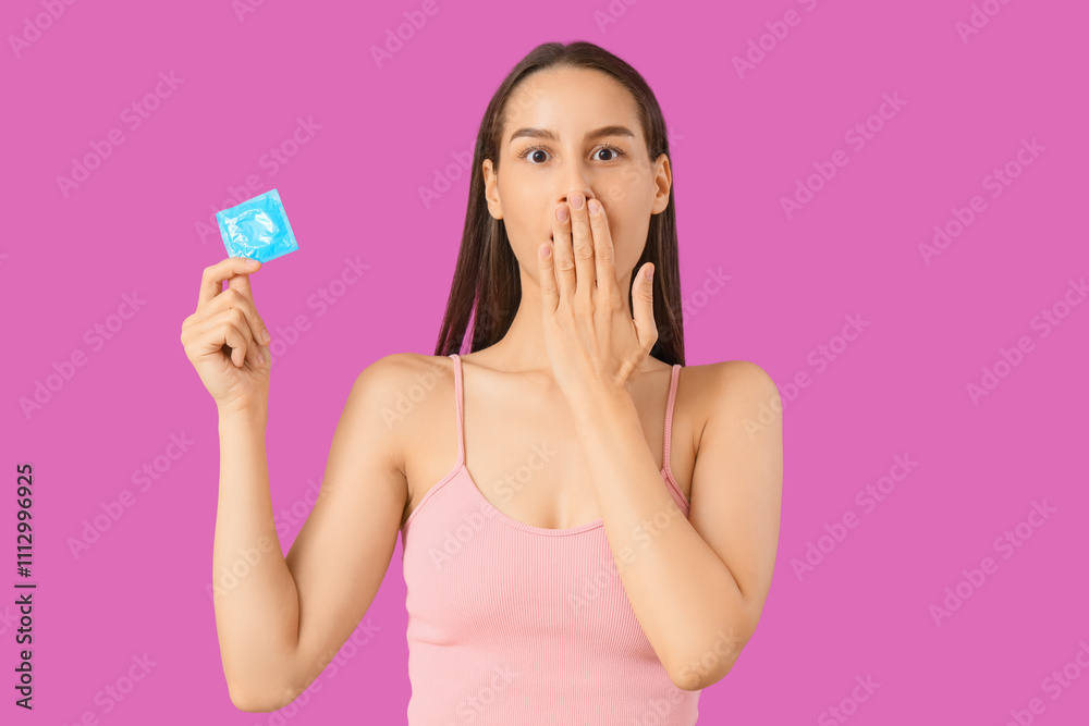 Shocked young woman with condom on purple background