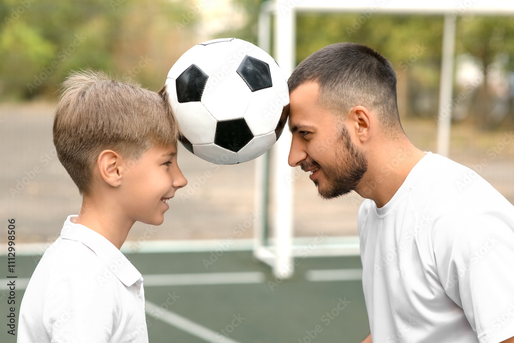 Father and his son with ball on soccer pitch