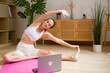 © mahalo studio/Stocksy - woman doing online yoga class at home stretching on a mat