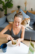 © mahalo studio/Stocksy - woman preparing matcha tea with her shiba inu dog resting on a couch