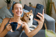 © mahalo studio/Stocksy - Woman taking selfie with shiba inu dog on sofa