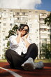 © Yuliia - Woman in sunglasses and headphones sits outdoors on a track, enjoying a sunny day and her favorite tunes, vertical photo.