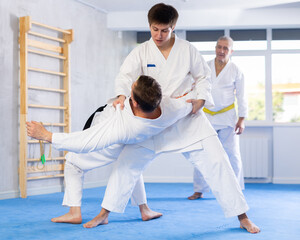 Wall Mural - Two men practice grabbing and throwing sports mats during judo training under the guidance of an experienced elderly coach