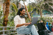 © Jimena Roquero/Stocksy - Traveling smiling man waiting at train station using laptop