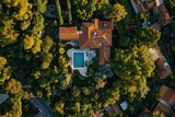 Aerial view of a luxurious house nestled in lush greenery, featuring a swimming pool and terracotta roof.