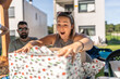 © Alvaro Lavin/Stocksy - Excited woman opening a christmas gift with friends outdoors