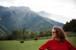 © Alina Hvostikova/Stocksy - Woman in red sweater enjoys scenic mountain view with grazing cows
