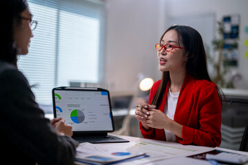 Wall Mural - Two women are sitting at a table with a laptop and a stack of papers