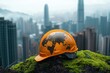 © SY - Orange hard hat with world map design, rests on mossy rock against city backdrop. Illustrates global construction, sustainable development, or international projects.