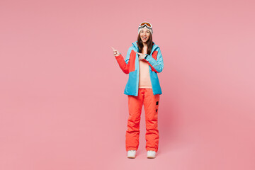 Poster - Full body skier young woman wear blue padded jacket ski goggles mask spend weekend winter season in mountains point index finger aside on area mock up isolated on plain pink background. Hobby concept.