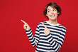 © ViDi Studio - Young smiling happy Caucasian woman wearing blue striped sweatshirt casual clothes pointing index finger aside on empty area mockup isolated on plain red background studio portrait. Lifestyle concept.