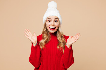 Canvas Print - Merry shocked surprised young woman wears red warm cozy knitted sweater hat posing spread hands isolated on plain pastel light beige background. Happy New Year celebration Christmas holiday concept.