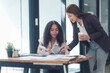© Kritdanai - Collaborative Success: Two young businesswomen, one African American and one Asian, engage in a productive meeting, reviewing documents and collaborating on a project.