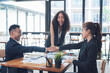 © Kritdanai - United in Success: A diverse team of business professionals in a modern office setting, their hands stacked together in a gesture of unity and collaboration. They are excited and happy.