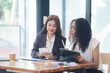 © Kritdanai - Collaborative Businesswomen: Two diverse businesswomen, one Asian and one Black, engage in a productive meeting, reviewing documents on tablets and notepads.