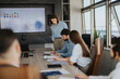 © qunica.com - A diverse team of business people engaging in a meeting with charts displayed on a screen. The atmosphere suggests teamwork and strategic planning.