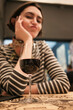 © Connect Images - Woman sitting at a table with a glass of red wine, looking pensive and tempted to drink the wine