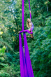 © Connect Images - Female aerialist performs an elegant pose on purple silk ribbons amidst a lush green forest background, USA