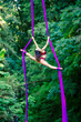 © Connect Images - Aerial performer executing a pose on purple silks amidst a lush green forest backdrop, USA