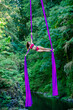 © Connect Images - Aerial silk performer demonstrating a pose in vibrant purple silks above a forested river, USA