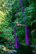 © Connect Images - Aerial silk performer executing a split while hanging from vibrant purple fabrics amidst a lush green forest setting, USA
