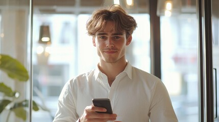 Fototapete - In a bright and contemporary office space, a focused young European man uses his smartphone, embodying professionalism and engagement in daily tasks. Sunlight enhances the modern ambiance