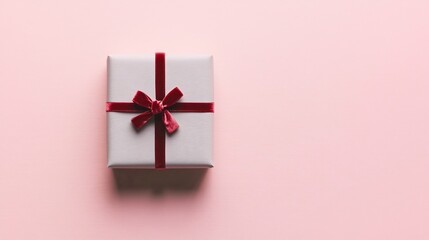 Poster - Elegant minimalistic photograph of a small gray gift box tied with a thin red velvet ribbon positioned against a plain soft pink background with ample copy space for text or design overlay
