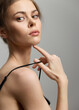 © SHOTPRIME STUDIO - Elegant young woman with a thoughtful expression, lightly touching her face, against a soft gray background. Beauty and fashion concept for portraits.