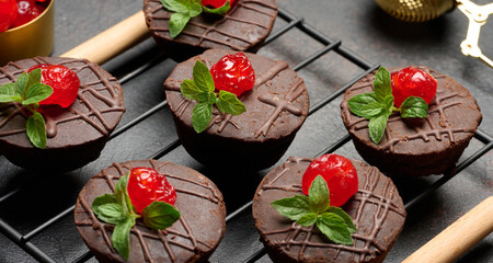 Wall Mural - Deliciously rich chocolate brownies garnished with vibrant cherries and mint leaves, resting on a black wire rack