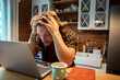 © Davor - Frustrated young man holding head while studying on laptop at kitchen table
