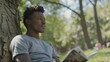 © StasySin - A young man is sitting on a tree branch reading a book. He is smiling and he is enjoying his time
