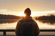 © c80 - An adventurer stands on a pier, facing the water as the sun rises; equipped with a backpack in cool morning air; experience of new day and possibilities unfolding.