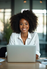 Poster - A smiling woman sits at her desk with an open laptop, wearing a white button-down shirt
