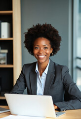 Poster - A woman sits at a desk with an open laptop in front of her in a professional setting