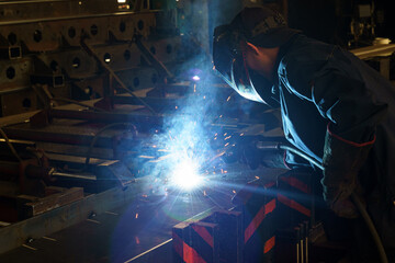 Poster - Skilled welder creating sparks in bustling workshop during evening shift