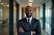 © miss irine - Confident African American businessman stands in office hallway. Wears suit, tie. Portrait photo shows pro, successful man. Modern business setting in background. Image suitable for business magazine