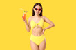 © Pixel-Shot - Beautiful young Asian woman in swimsuit and sunglasses with glass of cocktail on yellow background