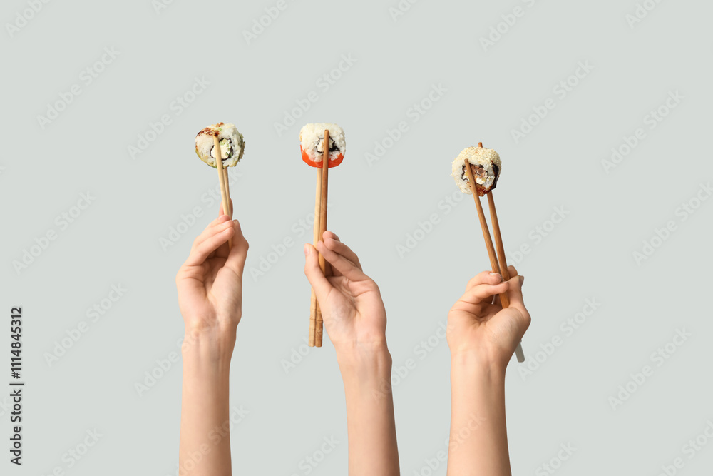 Female hands holding chopsticks with different tasty sushi rolls on grey background