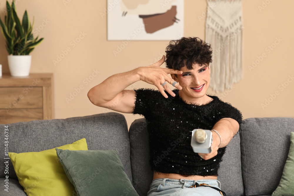 Young transgender woman with microphone sitting on sofa at home