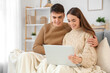 © Pixel-Shot - Loving young happy couple with plaid and laptop sitting on sofa at home