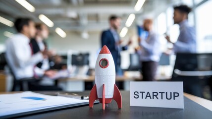 Poster - A model rocket symbolizes innovation in a startup office setting with professionals networking.