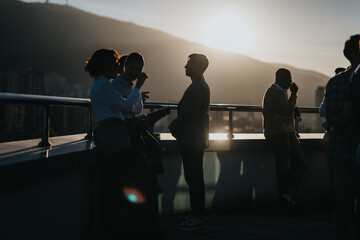 Wall Mural - A diverse group of business colleagues brainstorm on a high tower balcony as the sun sets, showcasing a multicultural collaborative atmosphere.